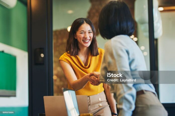Businesswoman shaking hands with client and smiling cheerfully in meeting room