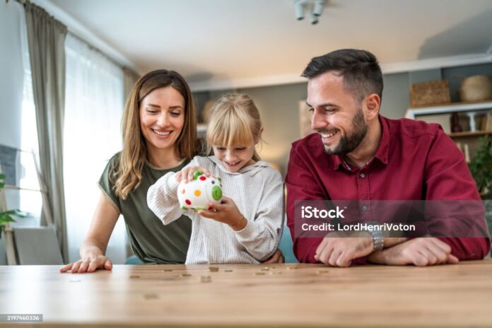 Cute excited daughter shaking coins out of a piggy bank at home